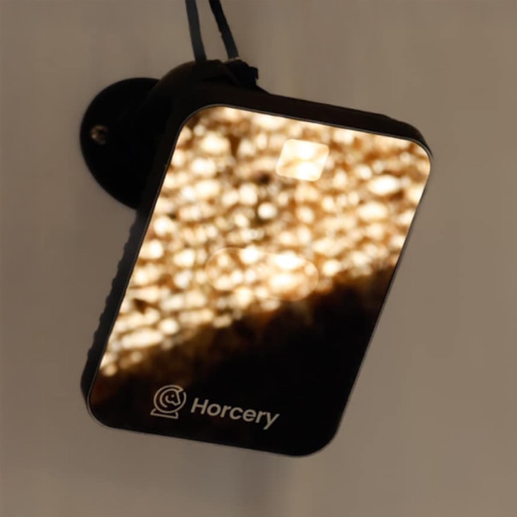 A Horcery AI Stall Monitor mounted on a wall, illuminated with warm reflected light on its front-facing surface, showing the Horcery logo at the bottom.
